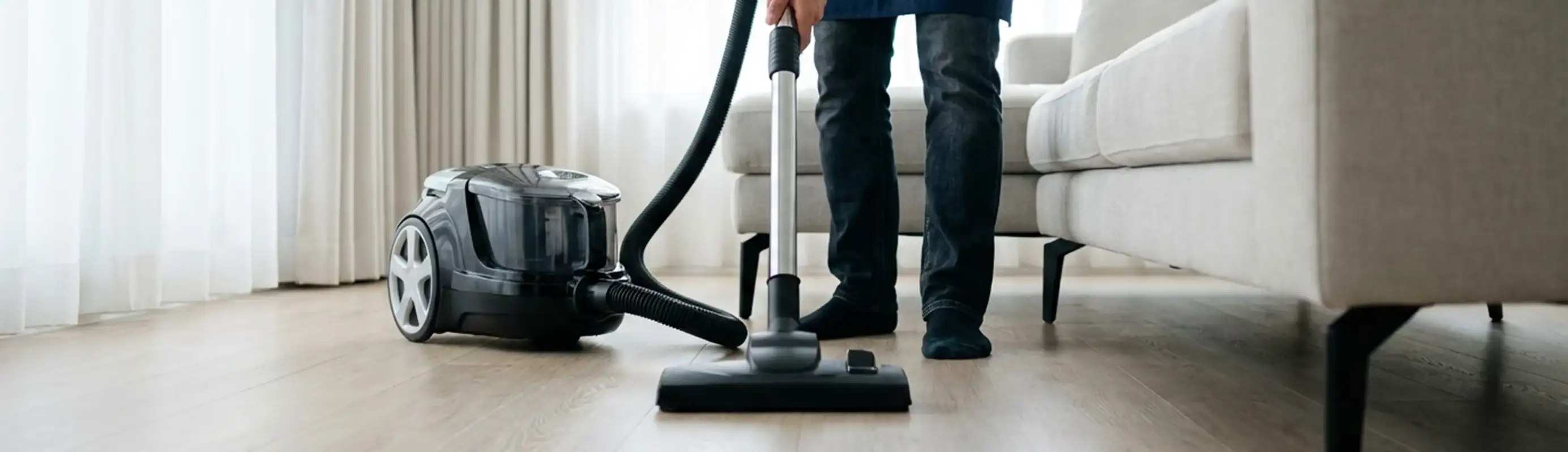 Professional house cleaner vacuuming a living room floor with a canister vacuum cleaner, Chandler, AZ.