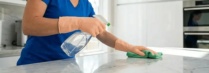 Maid service worker spraying and wiping a kitchen countertop with a microfiber cloth for sanitizing, Chandler, AZ.