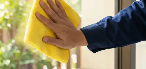 House cleaner wiping a glass window with a yellow microfiber cloth for streak-free cleaning, Chandler, AZ.